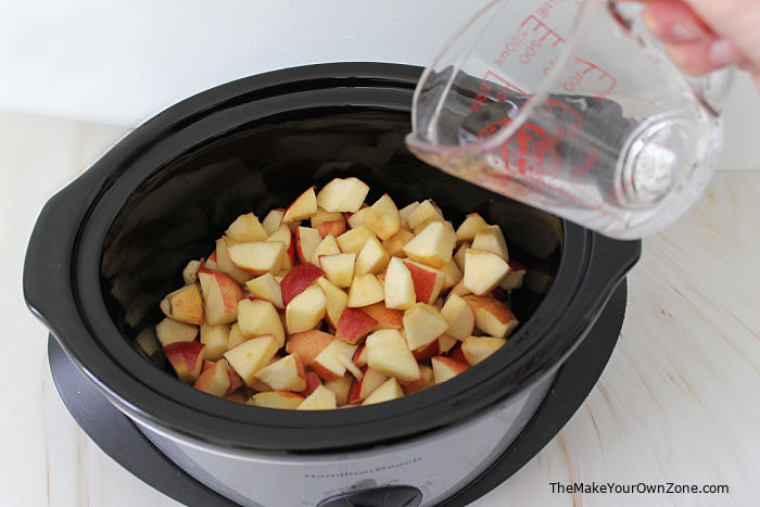 Adding water to a crockpot of apple chunks to make homemade applesauce