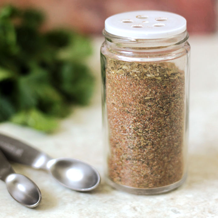 A jar of homemade 10-spice blend next to measuring spoons.