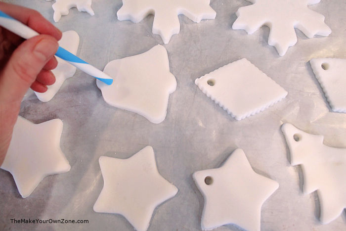 Using a straw to make a hole in the top of homemade white clay ornaments.