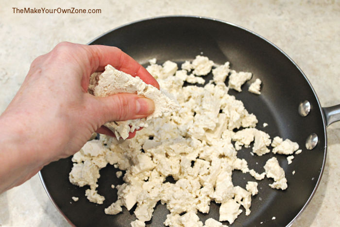 Crumbling tofu into a skillet to make a scramble